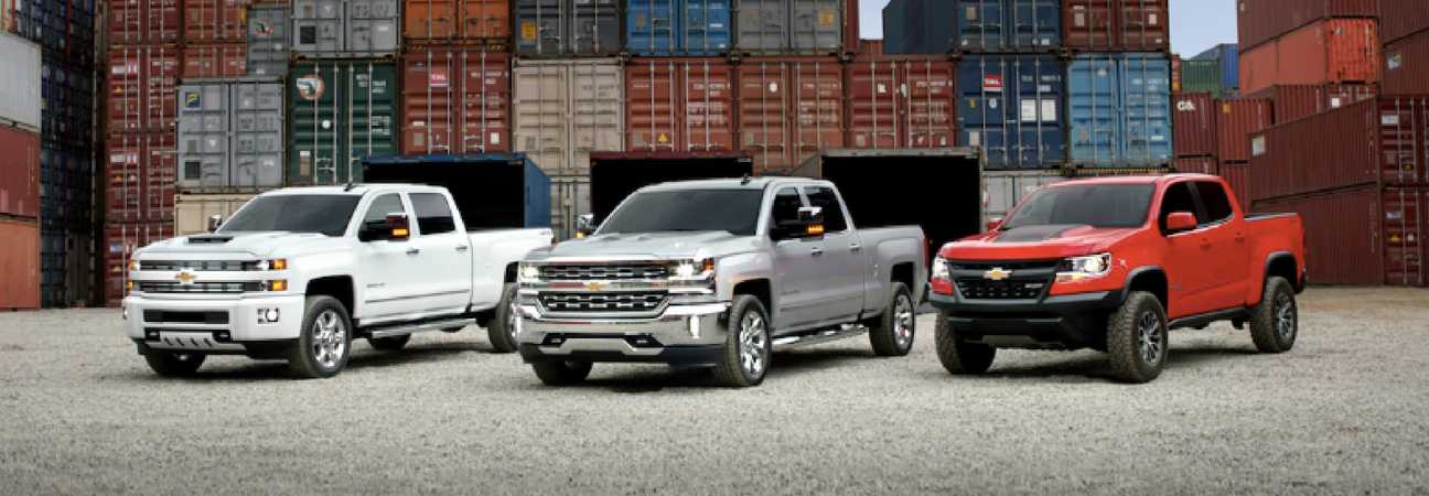 White Chevy Silverado, silver Chevy Silverado, and red Chevy Colorado lined up left to right at a freight yard